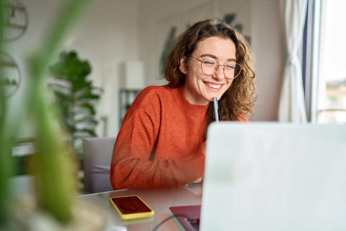 Eine junge Frau schaut in den Laptop, neben ihr liegt ein Handy. 